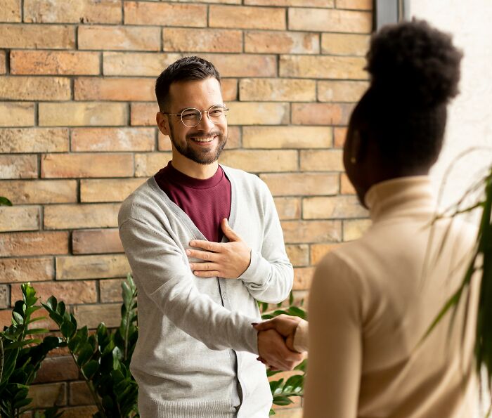 Man smiling and shaking hands with a woman, demonstrating real-life cheat codes for effective social interactions.