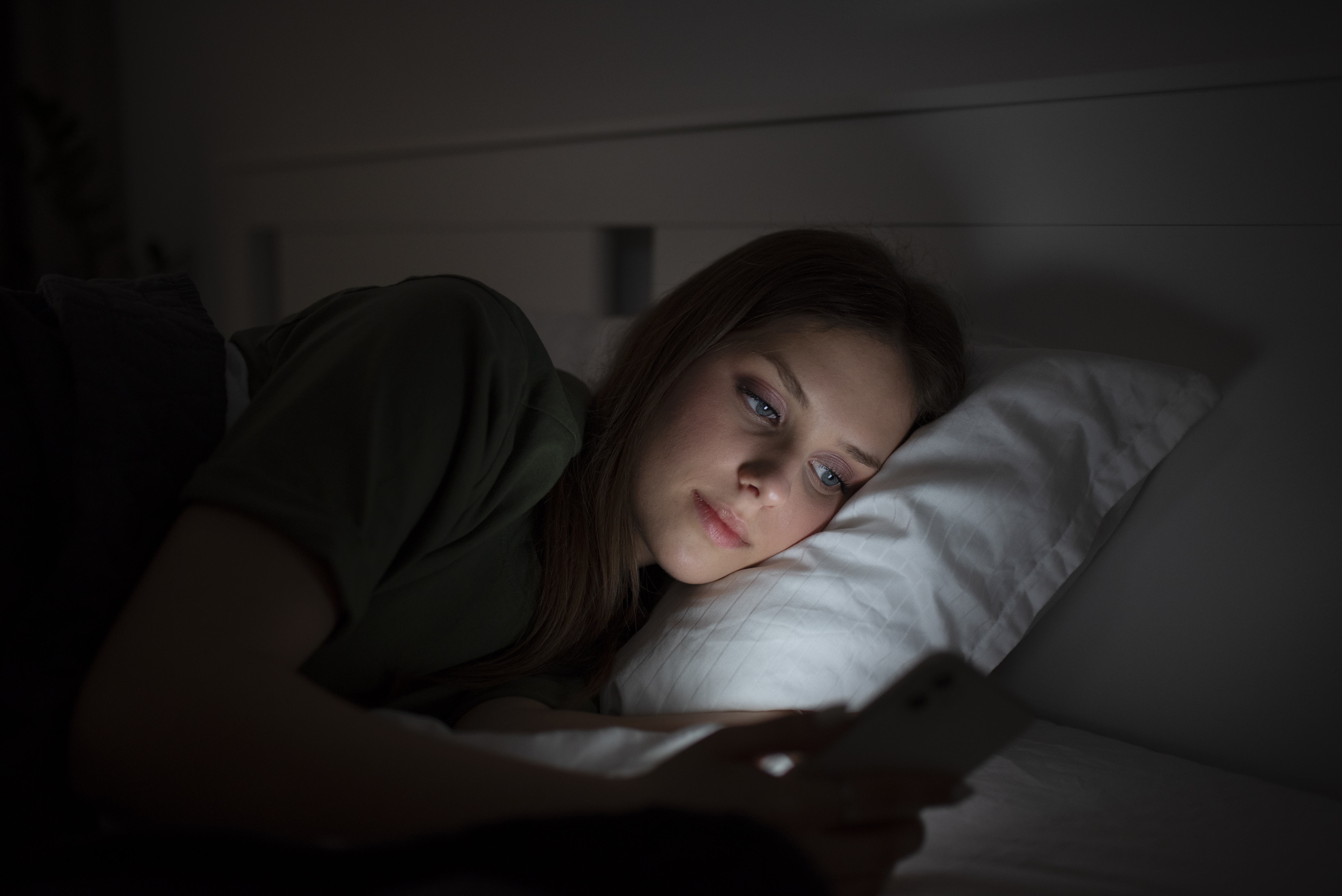 Young woman lying in bed at night, looking at her phone with a sad expression, reflecting on a heartbreaking cancer diagnosis.