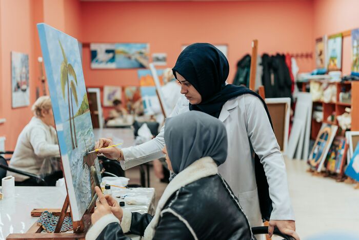 Woman in a black hijab guiding another person painting a beach scene, highlighting small decisions that changed life unexpectedly.