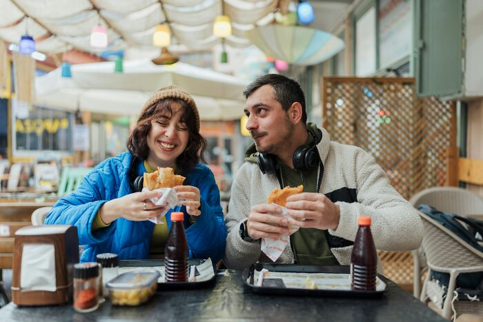 Couple enjoying sandwiches at a casual outdoor cafe, reflecting on small decisions that changed their lives.
