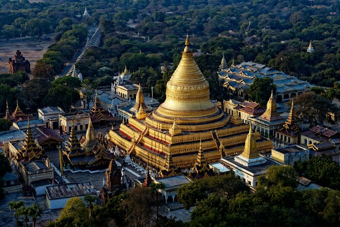 Aerial view of an ancient golden pagoda surrounded by historic buildings and lush greenery at a forgotten tourist destination.