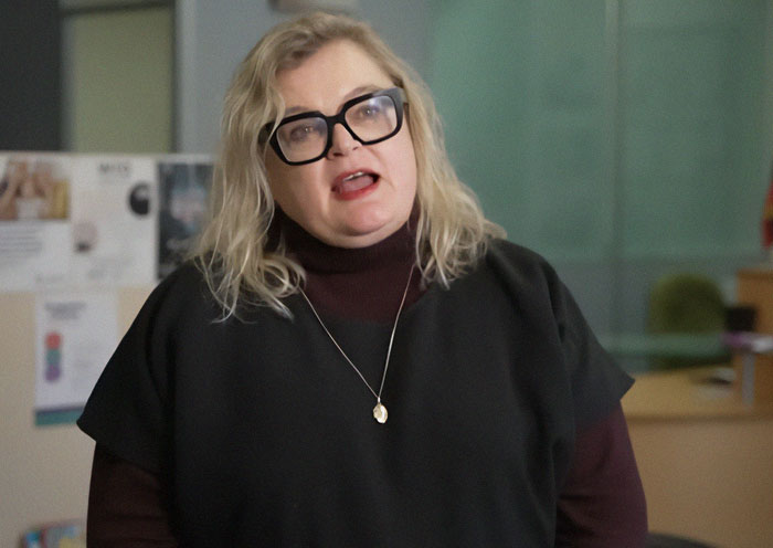 University professor with glasses speaking about women and men in domestic violence debate indoors.