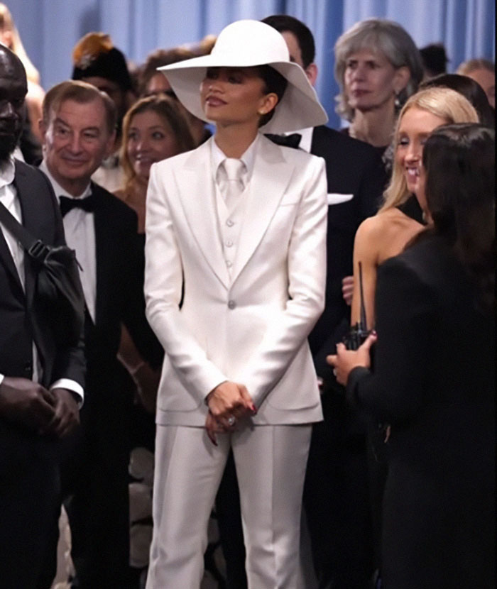Zendaya dressed in white suit and hat, reacting to Diana Ross upstaging her at the Met Gala red carpet event.