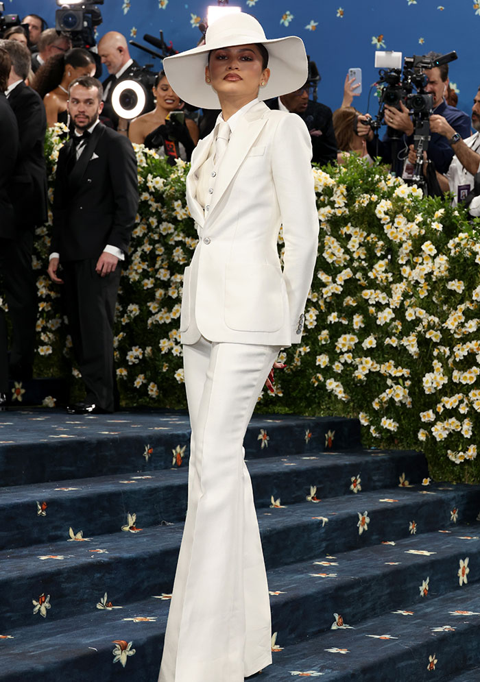 Zendaya posing in a white suit and hat on the Met Gala red carpet, capturing reactions to Diana Ross upstaging her.