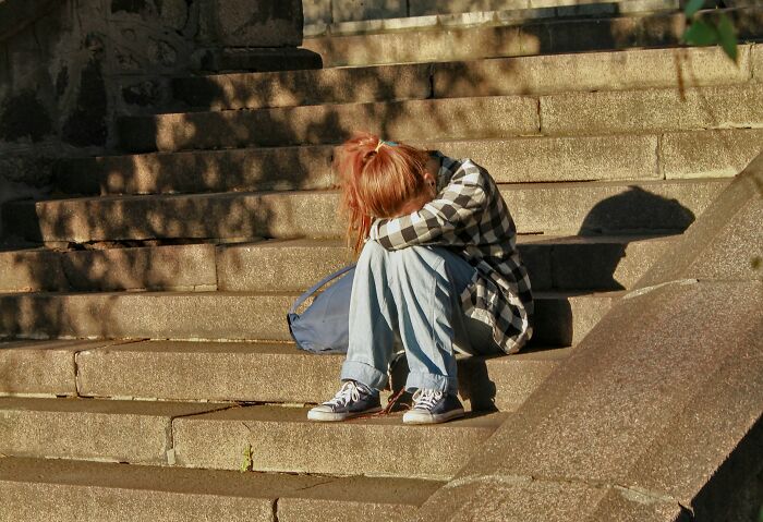 A young person sitting alone on stone steps, head down, conveying feelings of soul-crushing words from parents.