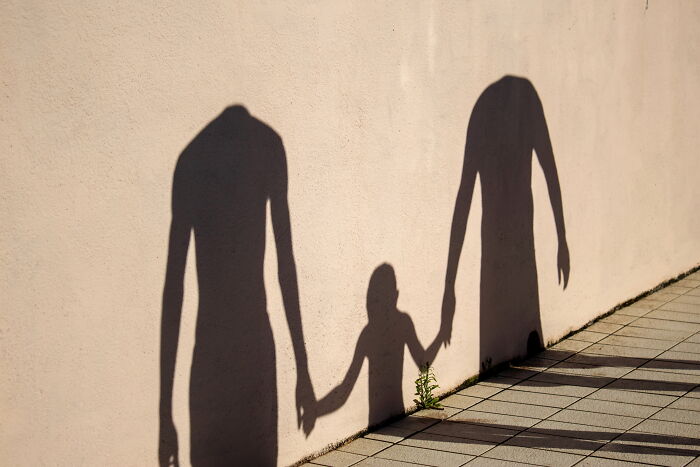Shadows of two adults and a child holding hands cast on a wall in a perfectly-timed street photo by Luca Regoli.