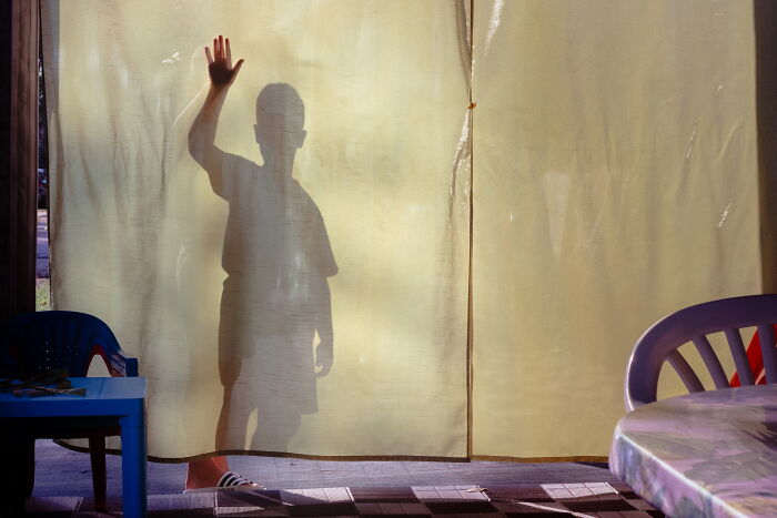 Shadow of a child waving behind a curtain, capturing a perfectly-timed street photo by Luca Regoli.