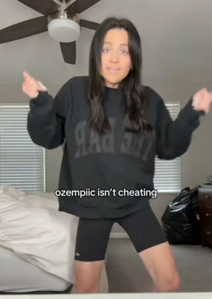 Woman wearing black sweatshirt and shorts discussing weight loss and Ozempic effects in a bedroom setting. Woman wearing black sweatshirt and shorts discussing weight loss and Ozempic effects in a bedroom setting.