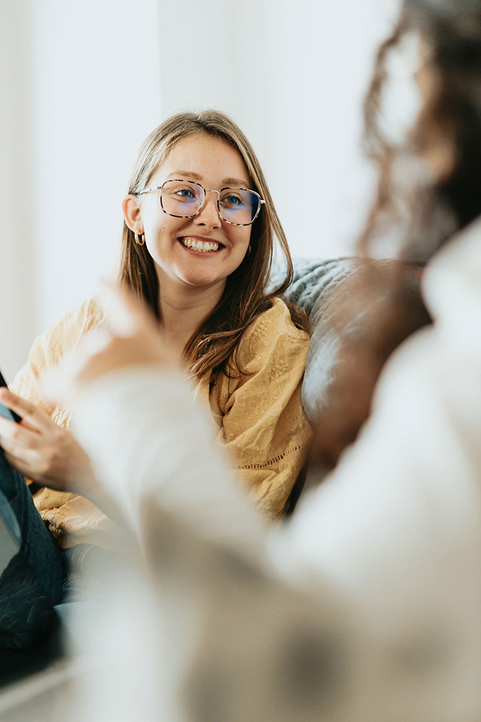 Smiling woman with glasses casually sitting on a couch during a conversation about cousin insulting her wedding and clapping back.