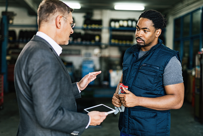 Man in a business suit advising a worker about punctuality and sticking to his schedule in a workshop environment.