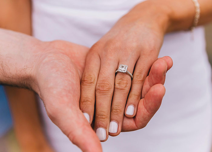 Close-up of a man holding a woman's hand with a diamond engagement ring, symbolizing a memorable proposal moment. Close-up of a man holding a woman's hand with a diamond engagement ring, symbolizing a memorable proposal moment.