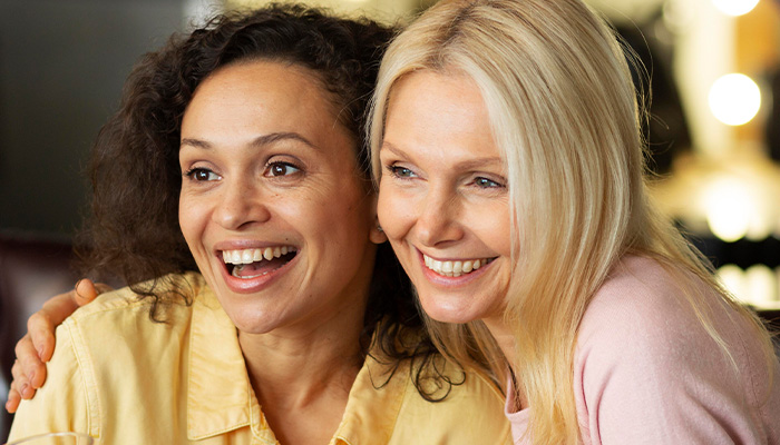 Two women smiling together, representing a woman setting boundaries with her friend about hosting a toddler.