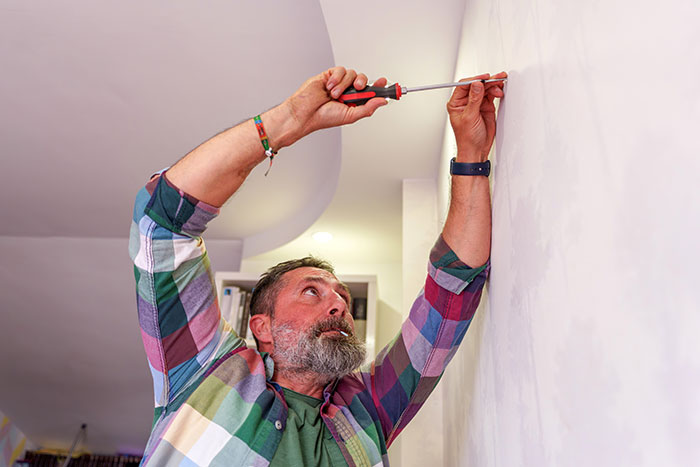 Man fixing wall with screwdriver, illustrating compliance and landlord dispute in a home maintenance setting.