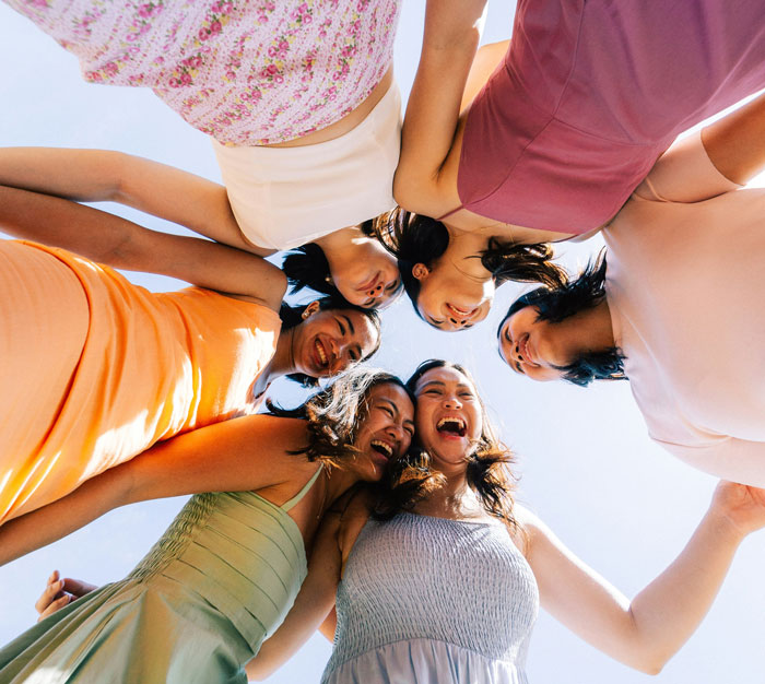 Group of women in colorful dresses standing in a circle outdoors, depicting a man hiring a PI about his partner.