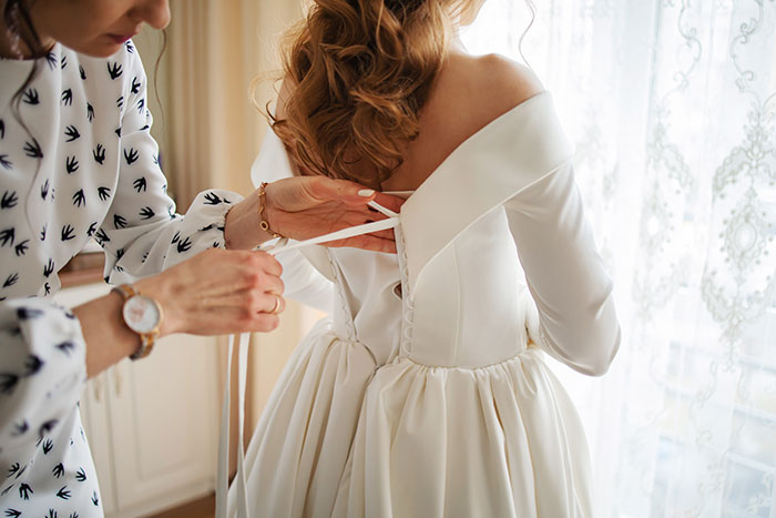 Woman trying on wedding dress with help, showing tension over wedding dress ruined by mother-in-law demand.