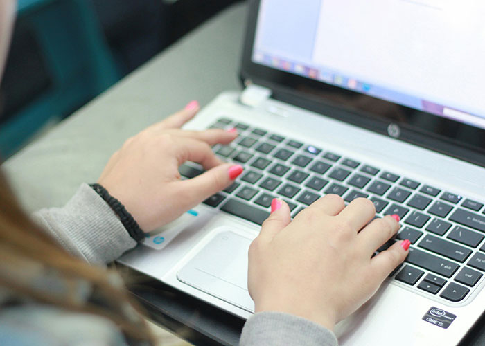 Hands with painted nails typing on a laptop keyboard, illustrating a mom assuming neighbor will babysit tantrum.