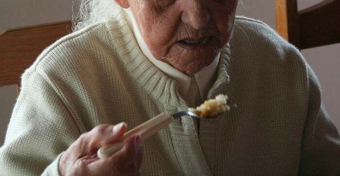 Elderly person in a beige sweater eating food, representing doctors sharing shocking discoveries made during autopsies