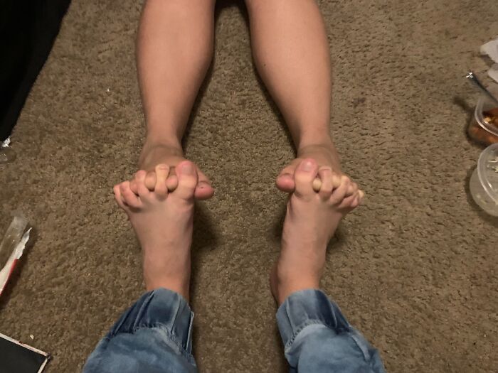 Two people sitting on a carpet with their toes intertwined in a weird gesture showing unusual couple behavior.