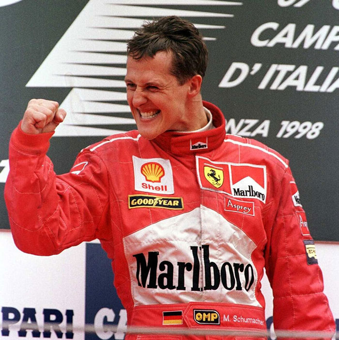 Michael Schumacher celebrating a race win in Ferrari racing suit, highlighting the F1 legend's health update.