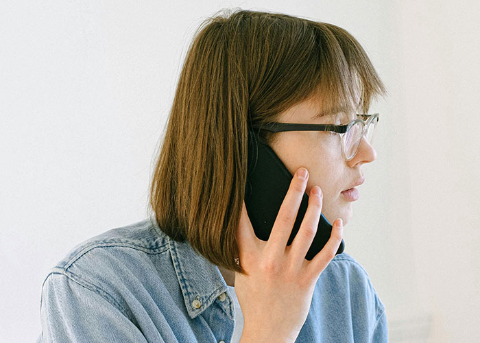 Woman in glasses and denim shirt making a phone call, reflecting awkward moments from painful and awkward dates.