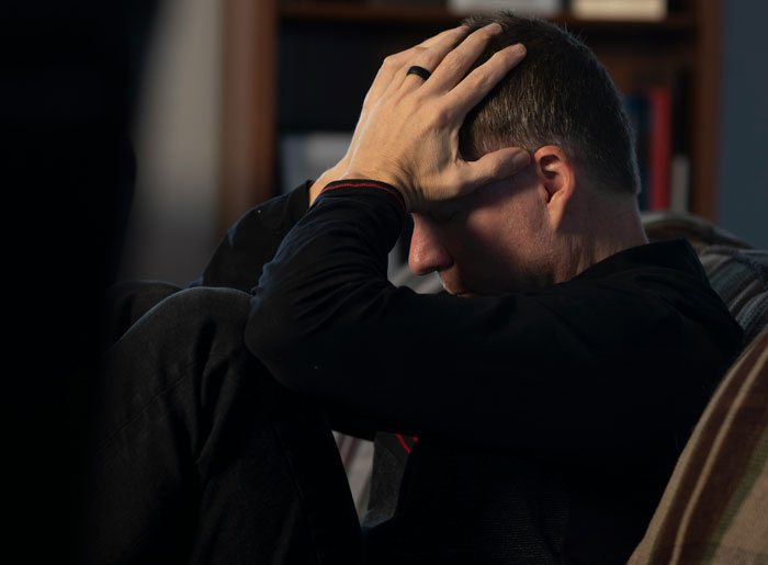Man sitting on a couch holding his head in distress, reflecting on the biggest mistake of his life.