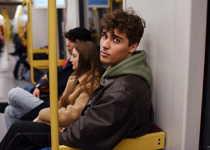 Young man in a leather jacket sitting on public transport looking at camera, capturing surreal and relatable commute moments.