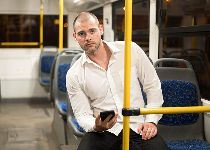 Man in white shirt holding phone, sitting on public transport, capturing the unsettling and surreal moments of a commute.