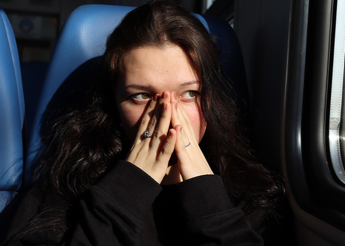 Young woman on public transport covering her face with hands, looking anxious and overwhelmed by the chaotic experience