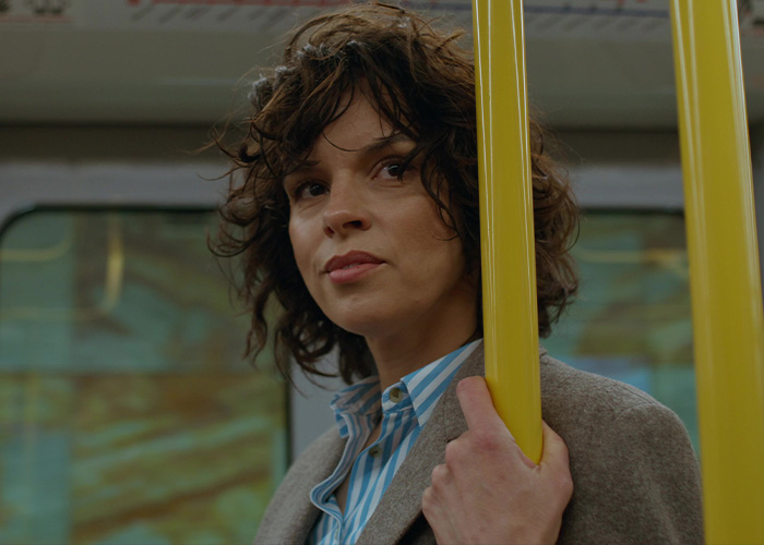 Person with curly hair holding a yellow pole inside public transport, capturing a surreal moment on the commute.
