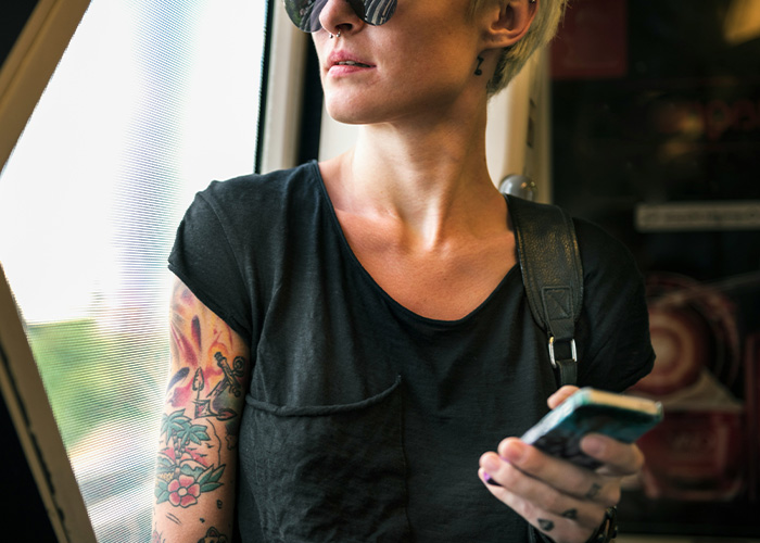 Young woman with tattoos looking out the window while holding phone on public transport, capturing a surreal moment.