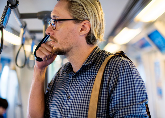 Man wearing glasses and checkered shirt standing in crowded public transport holding strap during commute.