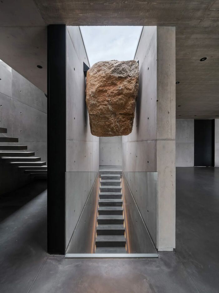 Modern concrete stairs with glass sides and a large rock suspended above, showcasing a death stairs design concept.