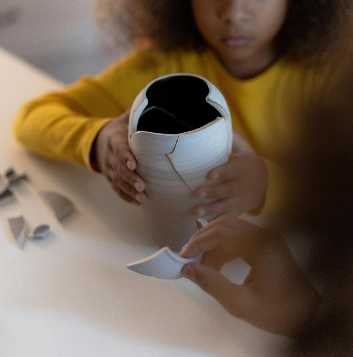 Child in yellow sweater holding broken vase pieces, symbolizing challenges in paying for college secrets.