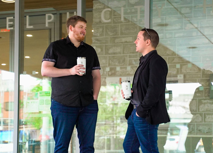 Two millennials having a casual conversation outdoors holding coffee cups, reflecting lies they were told growing up.
