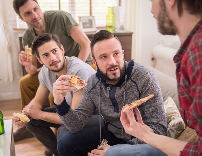 A group of friends eating pizza and talking indoors, capturing the moment about not letting a buddy crash at the place. A group of friends eating pizza and talking indoors, capturing the moment about not letting a buddy crash at the place.