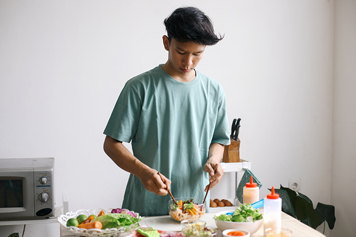 Young man making lunch only for himself in a kitchen, reflecting moment of mom guilt-trip about siblings.