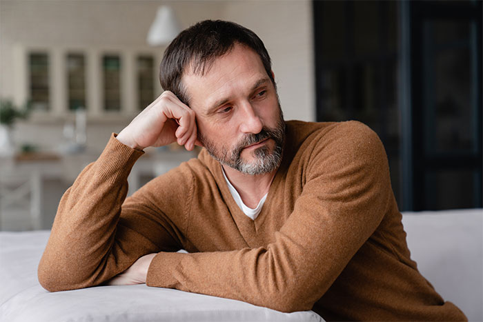 Pensive middle-aged man in brown sweater reflecting on family issues and years of neglect at home.