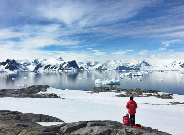Two travelers in red jackets overlooking icy waters and snow-covered mountains at one of the scariest places around the world.