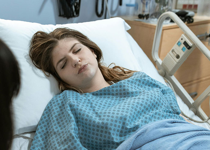 A woman resting in a hospital bed during labor while a dad supports her inside the birthing room for the first time.