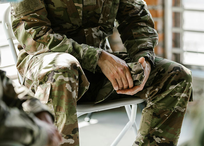 Soldier in camouflage uniform sitting and holding their hands, representing a take one for the team moment in military context.