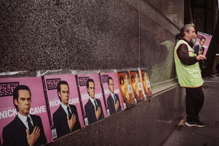 Candid street photo showing a man holding magazine issues lined up against a city wall.