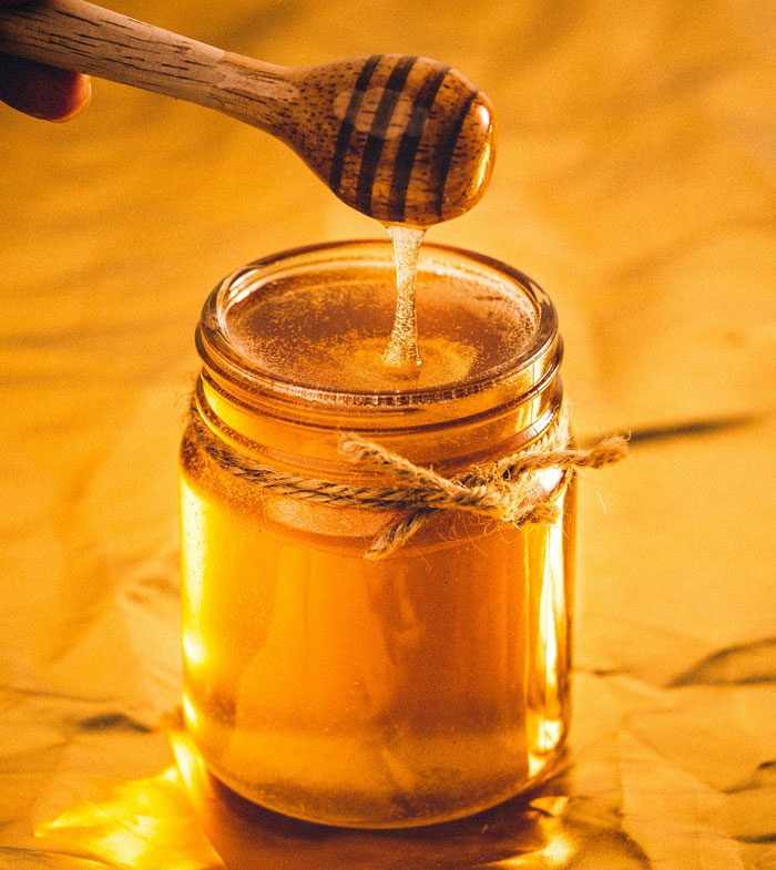 Jar of honey with honey dipper dripping honey, illustrating natural remedies from old wives' tales for health and wellness.