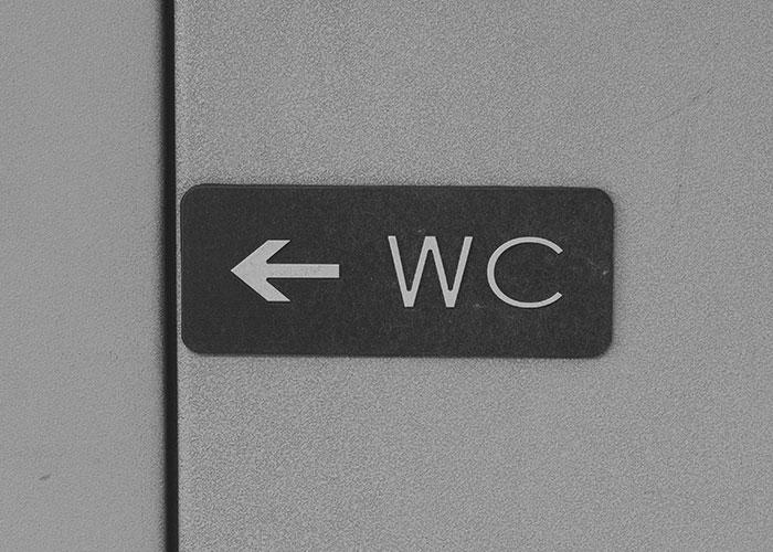 Black and white photo of a WC sign with an arrow pointing left, symbolizing wildest encounters of buffet workers.