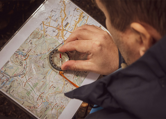 Person using a compass on a detailed paper map, showing people who still use obsolete navigation tools daily