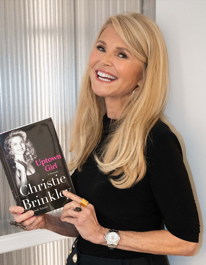 Blonde celebrity smiling and holding a memoir book, showcasing celebrities who look way younger than they actually are.