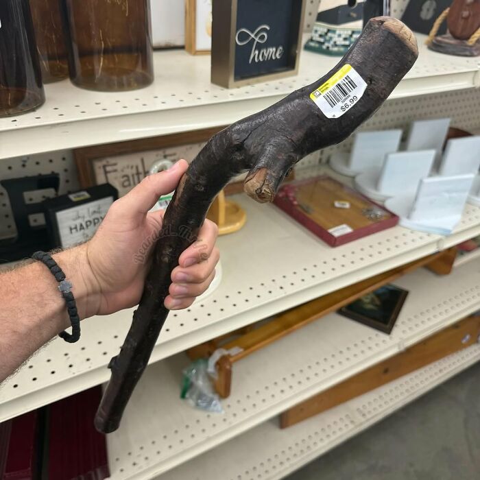 Hand holding a unique secondhand wooden walking stick with price tag in a thrift store aisle.