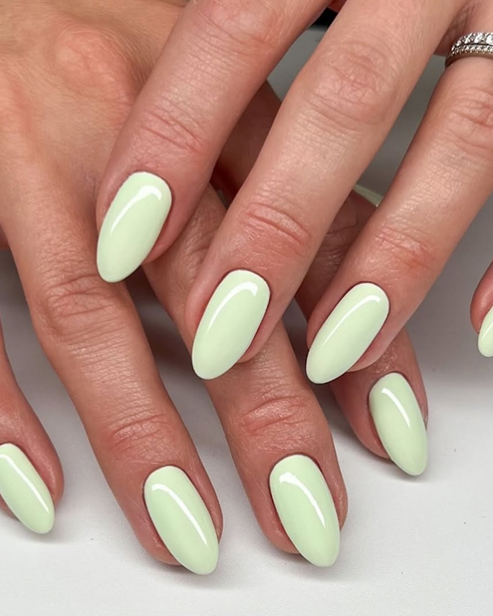 Close-up of glossy pastel green almond-shaped nails showcasing 2025 hottest summer nails style on well-groomed hands.