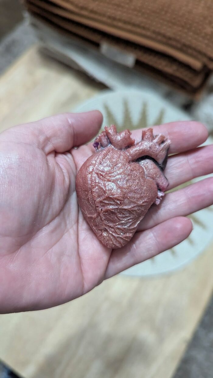 Hand holding a failed DIY craft project shaped like a glittery anatomical heart with rough texture and details.