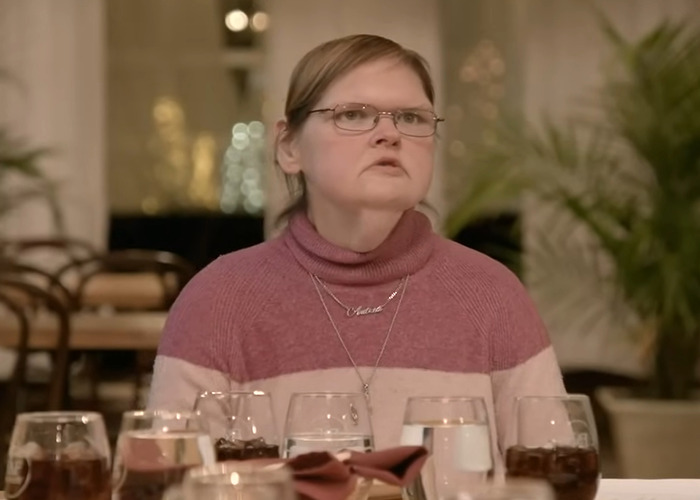 Woman from 1000-lb Sisters wearing glasses and a pink sweater sitting at a table with drinks in a dining setting. Woman from 1000-lb Sisters wearing glasses and a pink sweater sitting at a table with drinks in a dining setting.