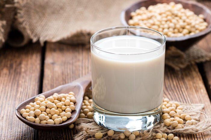 Glass of soy milk surrounded by soybeans on wooden table illustrating processed foods for weight loss.